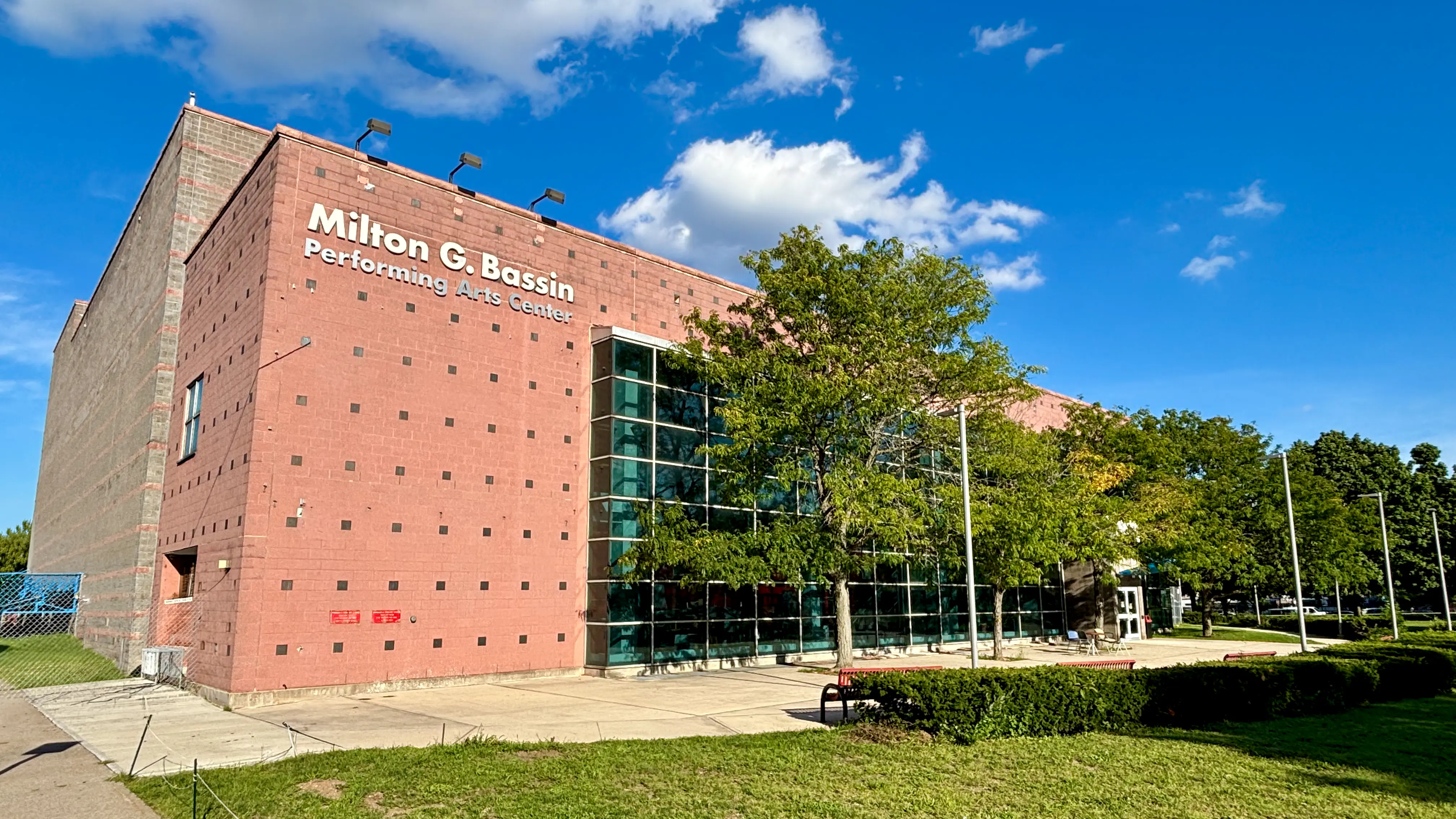 The exterior of the Milton G. Bassin Performing Arts Center, a large brick building with modern glass sections, under a bright blue sky.