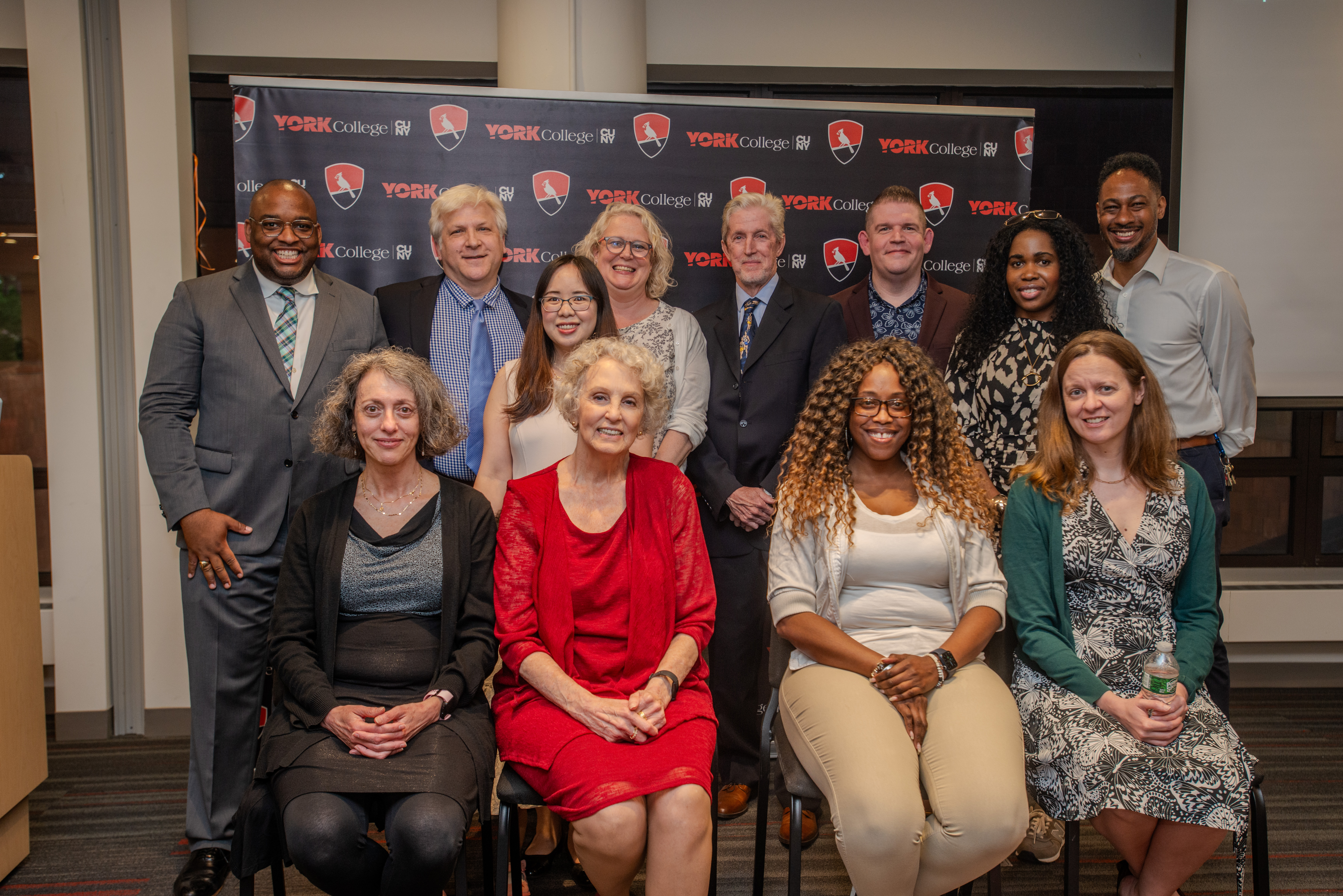 Health and Human Performance Faculty and staff in formal attire seated and standing in two rows before York College (CUNY) backdrop