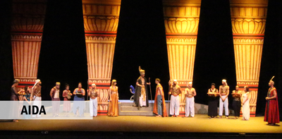 Cast members in ancient Egyptian costumes stand in front of four towering columns.